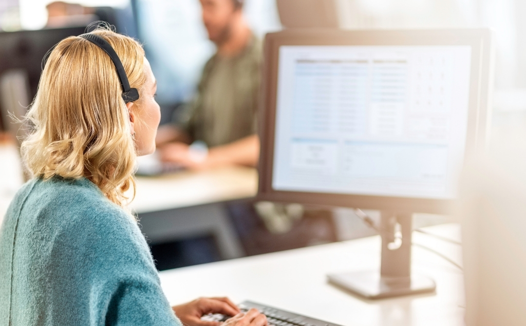 CRM-System Definition – Einleitungsbild: Frau mit Headset sitzt im Büro vor dem PC und tippt