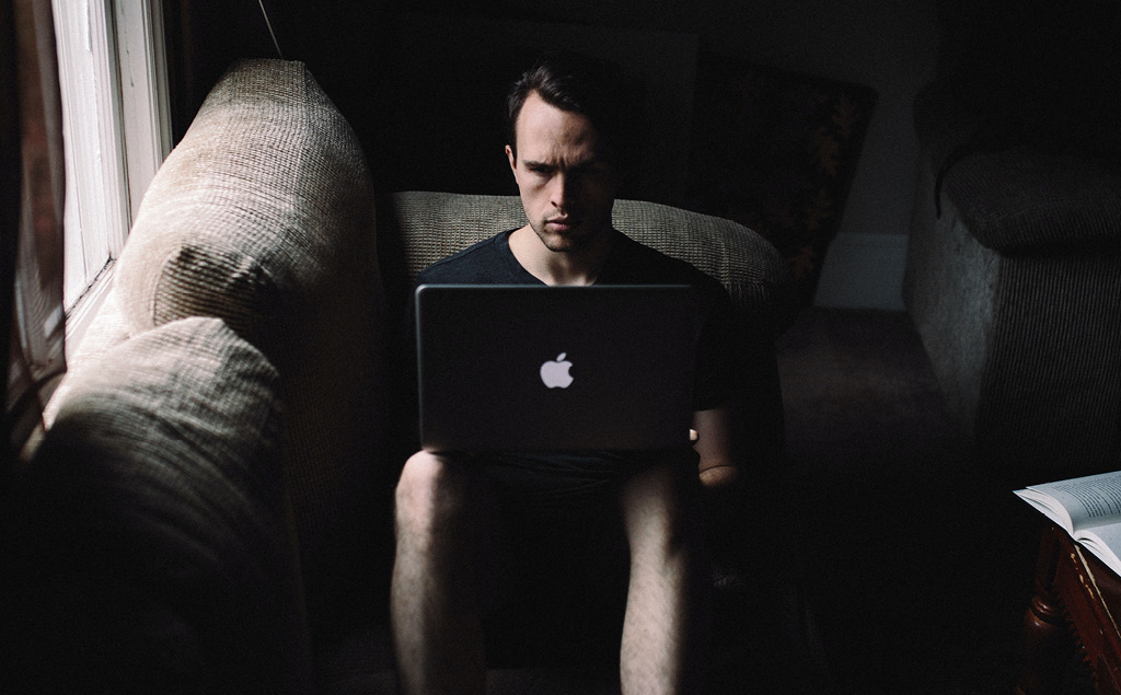 Mann sitzt grimmig mit Laptop und im Dunkeln auf dem Sofa